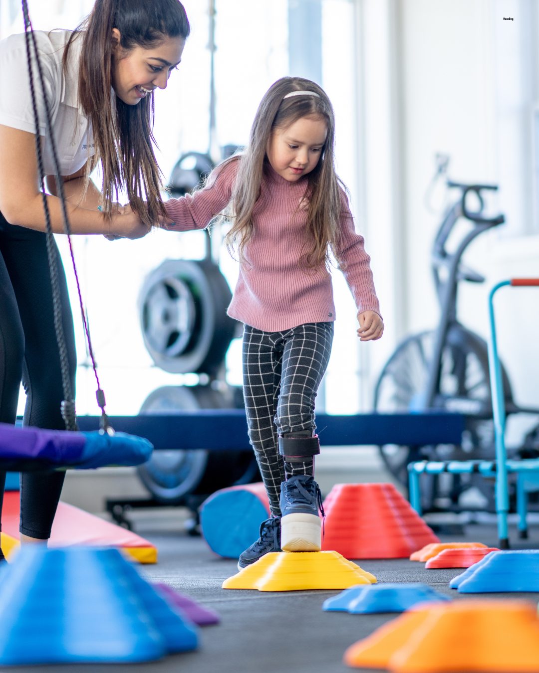 Pediatric therapist guiding a child through a movement and balance activity in the Vista clinic gym